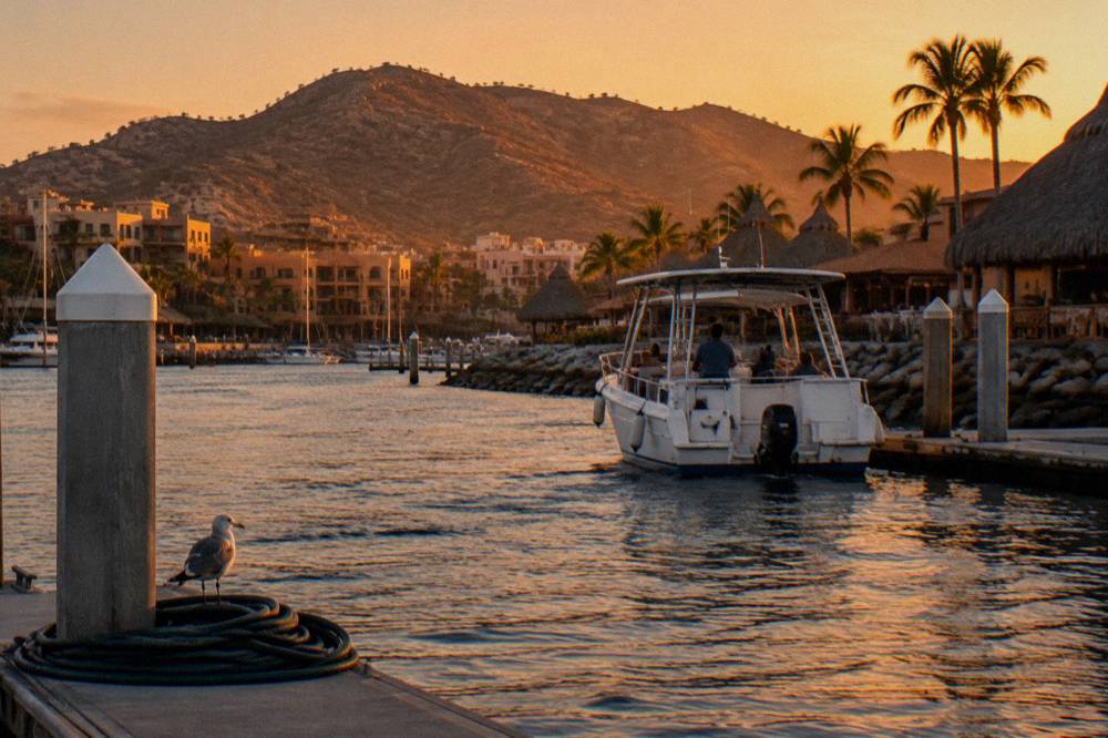 A small tour boat at golden hour with the Cabo San Lucas harbor and hills behind it